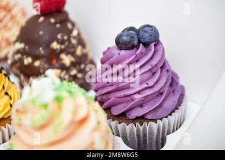 Petits gâteaux colorés avec glaçage à la crème tournoyée et baies. Pancakes à la vanille, au chocolat, aux myrtilles et aux framboises. Boîte de fête avec muffin aux myrtilles Banque D'Images