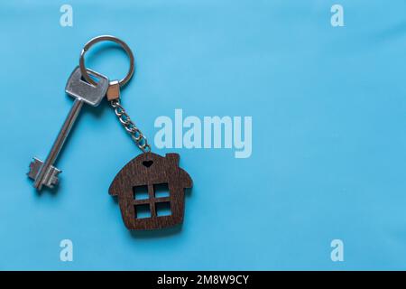 Clé avec porte-clés maison sur fond bleu coloré. Agent immobilier. Acheter une maison, un appartement. Banque D'Images