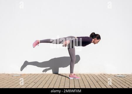 Femme sportive faisant guerrier trois yoga pose contre un mur blanc au soleil. Banque D'Images