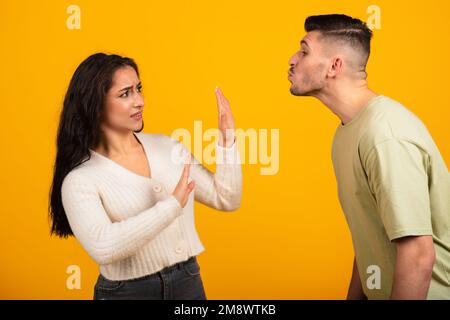 Millénaire arabe gars kising femme, dame faisant signe d'arrêt avec les mains, isolé sur fond orange Banque D'Images