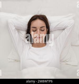 Vue de dessus d'une jeune femme dormant avec les mains sous la tête Banque D'Images