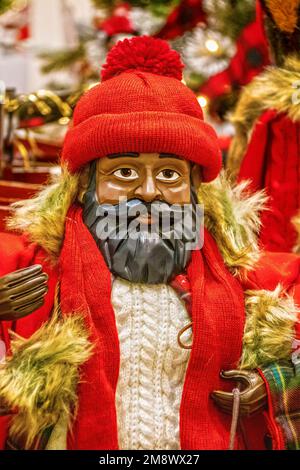 Poupée père noël en bois à la peau foncée avec barbe noire, chandail en maille torsadée, casquette rouge et manteau en fourrure Banque D'Images