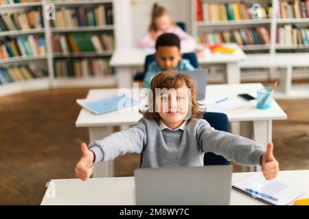 Concept d'éducation. Groupe de camarades de classe divers assis au bureau en classe, un garçon caucasien montrant les pouces vers le haut Banque D'Images