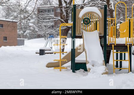 Terrain de jeu avec toboggan dans le parc sans enfants près des maisons, couvert de neige en hiver Banque D'Images