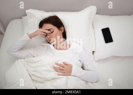 Agacé jeune femme couché dans le lit avec un smartphone sur un oreiller Banque D'Images