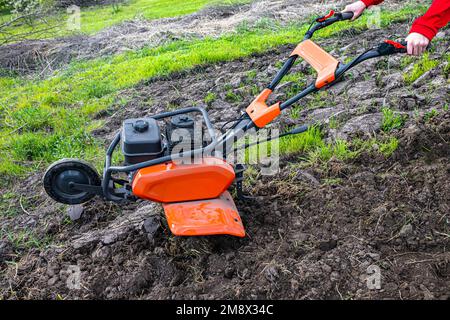 Cultivateur à moteur avec une roue avant relevée et un sillon inséré dans le sol pendant le labourage du champ avant de semer des semences et de planter des semences Banque D'Images