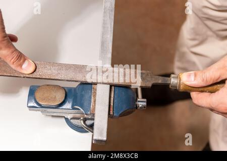 Man travaille avec un tuyau en fer ou une lime en aluminium métallique striée dans un étau sur une table d'établi dans un atelier de garage, faites-le soi-même concept. Banque D'Images