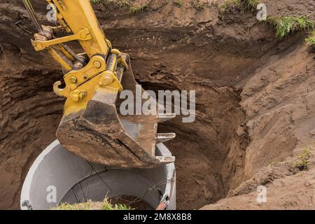 Pelle hydraulique avec un godet, s'abaissant dans la fosse sur des câbles en acier anneau d'égout en béton. Construction ou réparation d'un égout. Banque D'Images