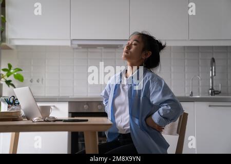 Femme asiatique fatiguée travailleur à distance souffrant de douleurs dorsales chroniques en travaillant à domicile Banque D'Images