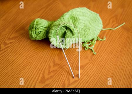 Chaussette tricotée, bille de fil et aiguilles à tricoter circulaires sur une surface de table en bois. Vue de dessus. Banque D'Images