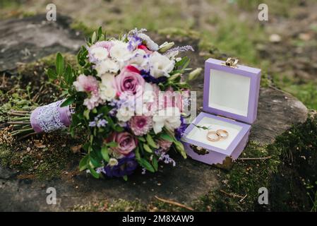 les anneaux de mariage dans une boîte à côté du bouquet se trouvent sur la souche Banque D'Images