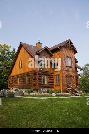 Vue latérale et arrière de la maison en rondins de style scandinave avec parement vertical en planches de bois et bardeaux de cèdre en été. Banque D'Images