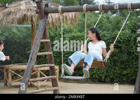 Bonne fille jouant sur la balançoire en bois dans l'aire de jeux. Banque D'Images