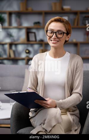 Belle souriante confiante jeune femme blonde avec un beau visage regarde la caméra. Psychologue ou femme d'affaires à la maison au bureau, heureux Banque D'Images