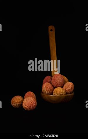 Lychees frais dans une cuillère en bois isolée sur fond noir Banque D'Images