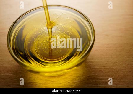 Gros plan d'une tasse en verre avec de l'huile d'olive extra vierge avec des bulles sur fond blanc Banque D'Images