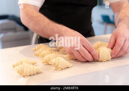 Mains d'un homme qui cuit de petits croissants à la maison, finissant des manipuler Banque D'Images