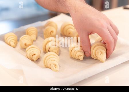 Mains d'un homme qui cuit de petits croissants à la maison, les préparant à mettre dans le four sur la plaque Banque D'Images