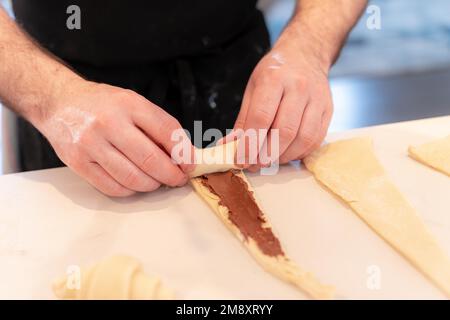 Les mains d'un homme qui cuit de petits croissants au chocolat à la maison, façonnant avec la pâte feuilletée Banque D'Images