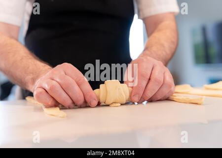 Les mains d'un homme qui cuit de petits croissants à la maison, se façonnant avec la pâte feuilletée Banque D'Images