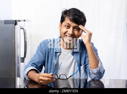 Un mâle indien avec des lunettes face au mal de tête assis à côté d'une table sur fond blanc Banque D'Images