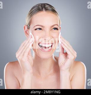 Le toner aide la peau à retenir l'humidité. Photo en studio d'une femme mûre attrayante utilisant des tampons de coton sur son visage sur un fond gris. Banque D'Images