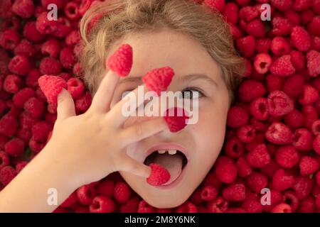 Framboise fraîche brute près du visage des enfants. Macro Raspberri. Vue de dessus des framboises de la collection. Enfant tenant des framboises sur ses doigts. Framboises Banque D'Images