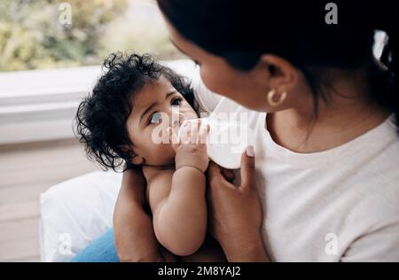 Quelle est ma fille préférée. une femme méconnaissable assise sur le lit à la maison et nourrissant sa petite fille d'un biberon. Banque D'Images