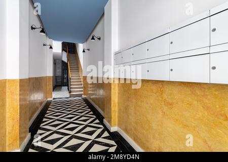Hall à l'entrée de la maison avec un long couloir, escaliers jusqu'au deuxième étage, sol en mosaïque de marbre noir et blanc, murs jaune vif, lampes en métal noir Banque D'Images