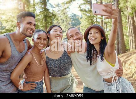 Tirer le meilleur parti du week-end ensemble. un groupe diversifié d'amis se tenant ensemble et prenant des selfies sur un téléphone portable tout en campant dans les bois. Banque D'Images
