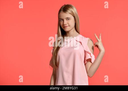 Portrait studio d'une belle fille blonde adolescente dans un t-shirt rose posant sur fond rose. Banque D'Images