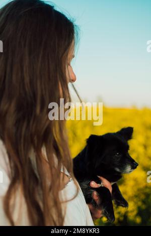 Une femme enceinte avec un petit chien noir dans la nature. Champ de colza Banque D'Images