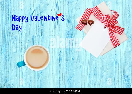 Tasse à café, boîte cadeau avec coeurs en chocolat et étiquette en papier vierge sur bureau en bois bleu avec texte pour la Saint-Valentin. Petit déjeuner le jour de la Saint-Valentin. Bonne Saint Valentin Banque D'Images