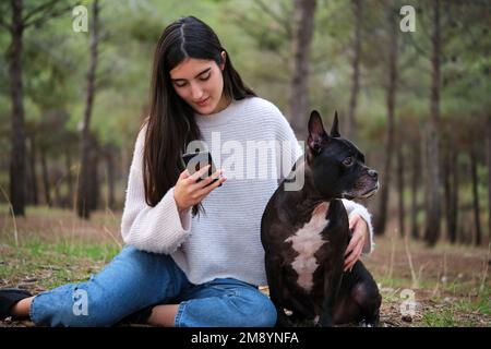 Jeune femme caucasienne utilisant le téléphone assis dans une forêt avec son chien . Banque D'Images