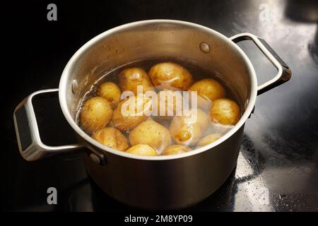 Pommes de terre avec pelage dans une casserole en acier inoxydable avec de l'eau bouillante sur le poêle, concept de cuisine saine, espace de copie, foyer sélectionné, profondeur étroite de fiel Banque D'Images