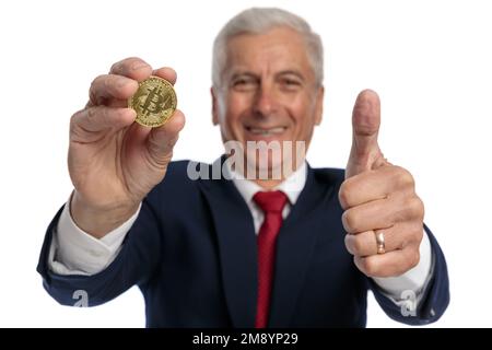 vieux homme d'affaires montrant un bitcoin et faisant des gestes qui est ok pour investir dans cette cryptocose Banque D'Images