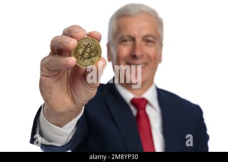 Un vieux homme d'affaires présentant un bitcoin à la caméra nous encourageant à investir dans des pièces de crypto Banque D'Images