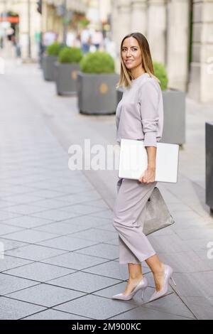 Femme d'affaires confiante et bien habillée avec un netbook qui se balade en ville Banque D'Images