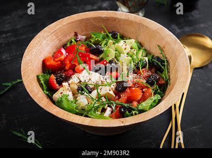 Salade fraîche avec avocat, tomates, mozzarella, poivrons doux et olives noires sur un bol en bois. Banque D'Images