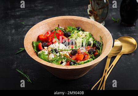 Salade fraîche avec avocat, tomates, mozzarella, poivrons doux et olives noires sur un bol en bois. Banque D'Images