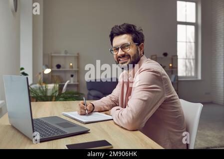 L'homme utilise un ordinateur portable, écrit, prend des notes, regarde un webinaire, s'entraîne ou participe à une leçon en ligne. Banque D'Images