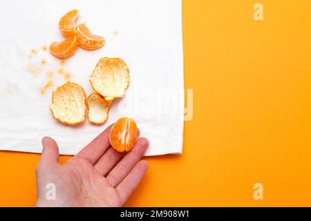 main féminine tenant des vêtements blancs avec taches de ditry de fruits mandarin sur fond orange Banque D'Images