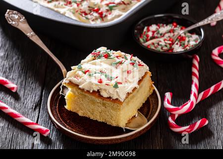 tranche de gâteau de noël en feuille de vanille avec glaçage à la crème fouettée garni de saupoudrés sur une pelle à gâteau sur une table en bois sombre, gros plan Banque D'Images