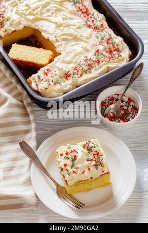 Tranche de gâteau de feuille de vanille avec glaçage à la crème fouettée, garni de saupoudrés du nouvel an sur une pelle à gâteau sur une assiette blanche, vue verticale Banque D'Images