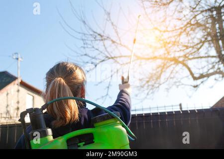 pesti de fumigation, lutte antiparasitaire. Défoquer la femme paysanne pulvérisant l'arbre avec un pulvérisateur manuel de pesticides contre les insectes dans le jardin de printemps. Agriculture et Banque D'Images