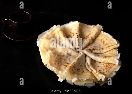 photo fines crêpes frites magnifiquement empilées sur une assiette avec une tasse de café sur un fond noir Banque D'Images