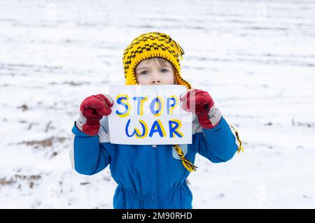 Portrait d'un garçon sérieux de 6 ans, avec un accent sur les yeux, protestant contre la guerre en Ukraine. Affiche contenant les mots Stop war écrits en bleu et yel Banque D'Images