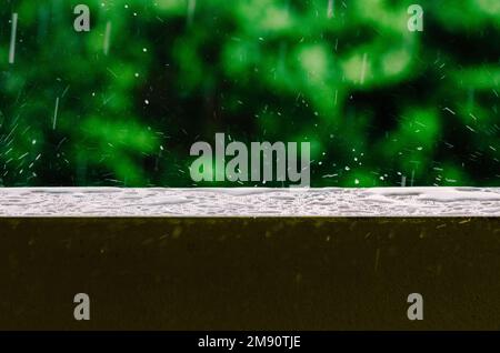 Prise de vue cinématographique de gouttes de pluie tombant du ciel gris sur la surface humide d'une balustrade de balcon, créant des ondulations dans l'eau plate Banque D'Images