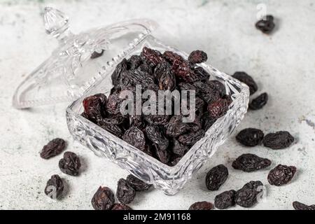 Raisins noirs séchés sur fond de pierre. Raisins secs dans un bol en verre. Variétés de noix. Une alimentation saine. gros plan Banque D'Images