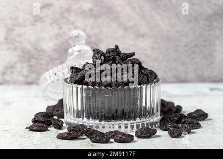 Raisins noirs séchés sur fond de pierre. Raisins secs dans un bol en verre. Variétés de noix. Une alimentation saine. gros plan Banque D'Images
